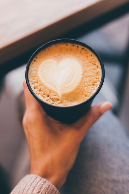 Plan de mains de femme tenant une tasse de café chaud avec un cœur en mousse.