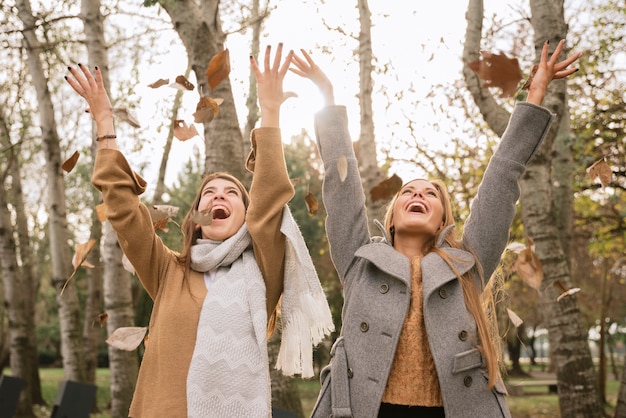 Plan moyen de deux femmes jouant avec des feuilles dans le parc