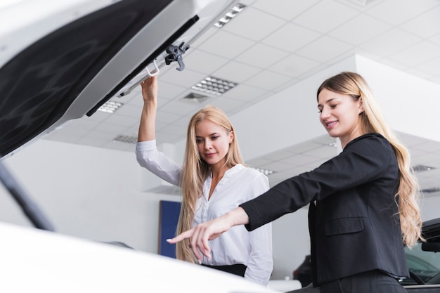 Plan moyen de femmes vérifiant le moteur d'une voiture