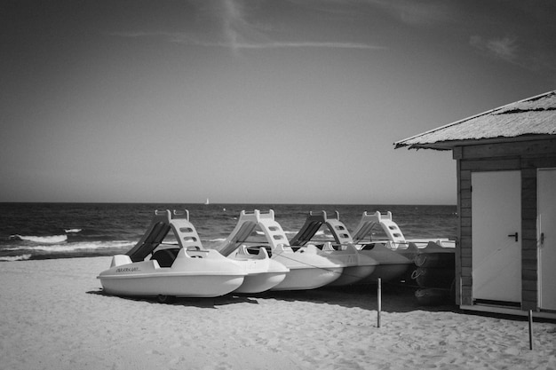 Photo gratuite plan en niveaux de gris d'embarcations ou de navires marins près d'une cabane sur une plage de sable