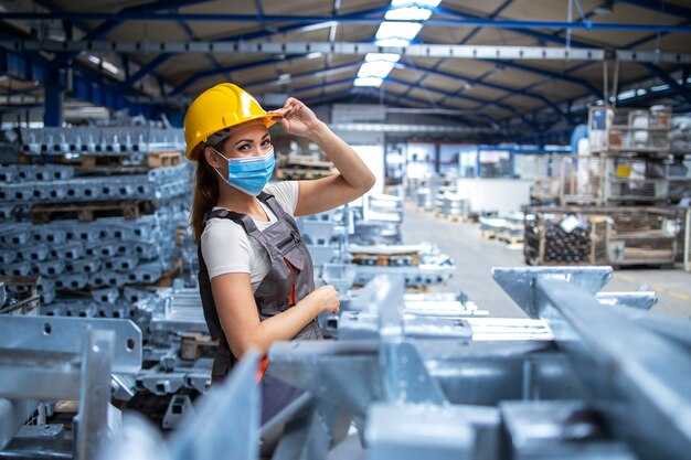 Plan d'une ouvrière d'usine en uniforme et casque portant un masque facial dans une usine de production industrielle