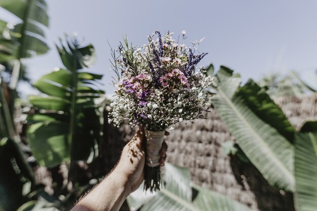 Plan d'une personne tenant un bouquet de mariée et de grandes feuilles vertes sur l'arrière-plan