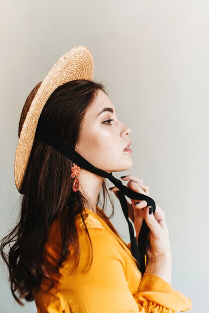 Plan de profil d'une fière européenne aux cheveux longs au chapeau orange. Femme aristocrate en plaisancier posant sur un mur isolé.