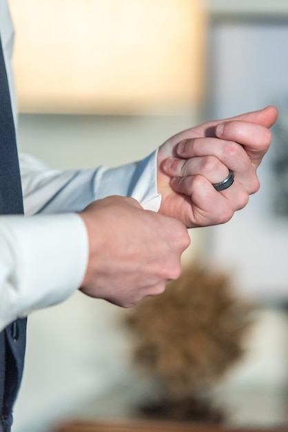 Photo gratuite plan rapproché vertical du marié portant sa bague de mariage et fixant ses boutons de manchette