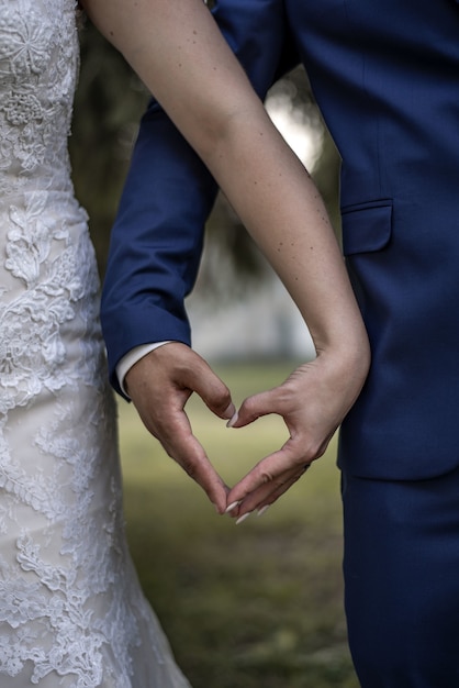 Plan rapproché vertical d'une mariée et d'un marié formant un coeur avec leurs mains