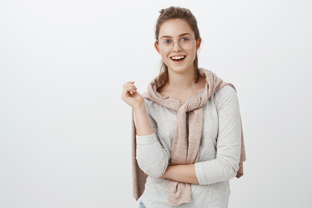 Plan à la taille d'une femme européenne amusée et sociable avec des cheveux peignés dans des verres et un pull noué sur le cou faisant des gestes pendant la conversation et souriant largement intéressé par la conversation