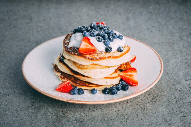 Plan vertical d'une assiette avec des crêpes gourmandes à la crème de fraises et de myrtilles