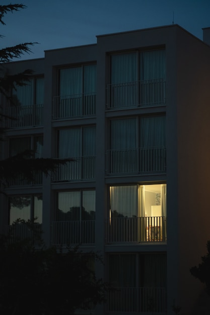 Photo gratuite plan vertical d'un bâtiment blanc moderne avec de la lumière sortant de l'une des grandes fenêtres du balcon