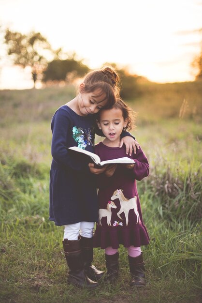 Plan vertical de deux adorables petites sœurs lisant la Bible dans le parc