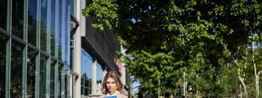 Photo gratuite plan vertical d'une femme d'affaires avec un dossier debout dans une rue près d'immeubles de bureaux portant un costume