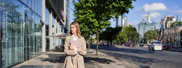 Plan vertical d'une femme d'affaires marchant dans la rue avec une tablette numérique allant au travail portant du beige