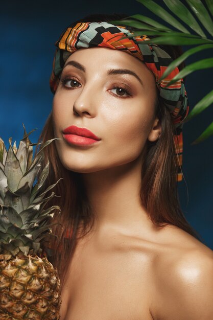 Plan vertical d'une femme nue avec des lèvres roses, un bandeau, des fruits.