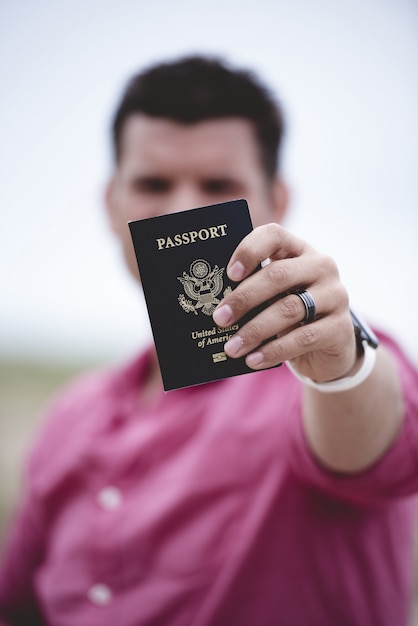 Plan Vertical D'un Homme Tenant Son Passeport Vers L'appareil Photo Avec Un Arrière-plan Flou