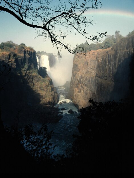 Plan vertical d'un jet d'eau au milieu des falaises et d'une cascade au loin