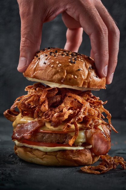 Plan vertical de la main d'un homme saisissant le pain supérieur du hamburger