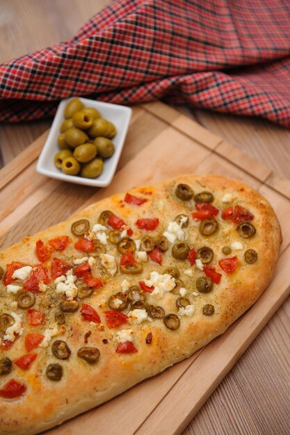 Plan vertical d'un pain cuit au four à base d'olives et de tomates et servi sur une planche de bois