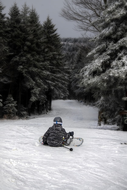 Plan vertical d'une personne assise sur la colline portant un snowboard