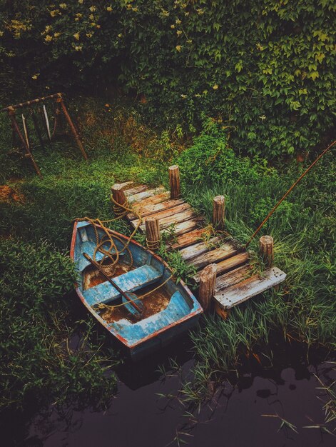 Plan vertical d'un vieux bateau dans l'eau près d'un quai en bois entouré de verdure