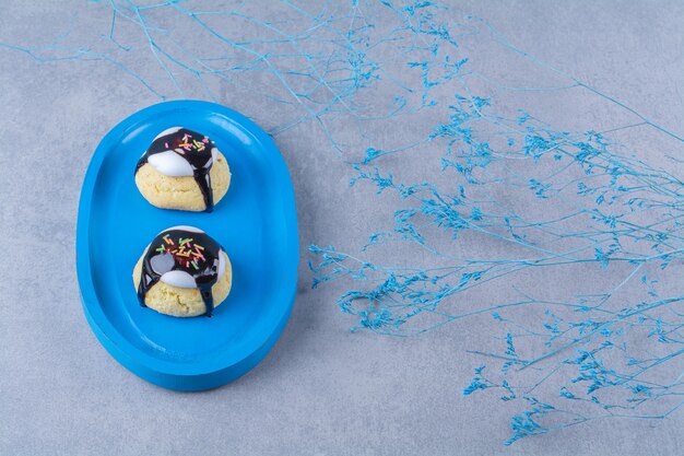 Une planche en bois bleue de biscuits sucrés avec des paillettes colorées et du sirop de chocolat.