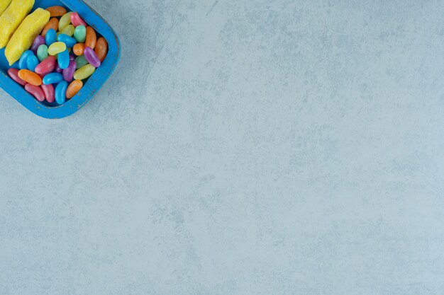 Une planche en bois bleue de bonbons à mâcher en forme de banane avec des bonbons aux haricots colorés