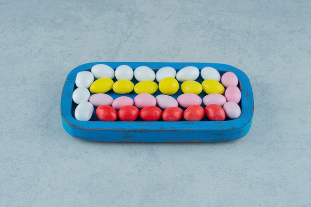 Une planche de bois bleue pleine de bonbons colorés sucrés ronds sur une surface blanche