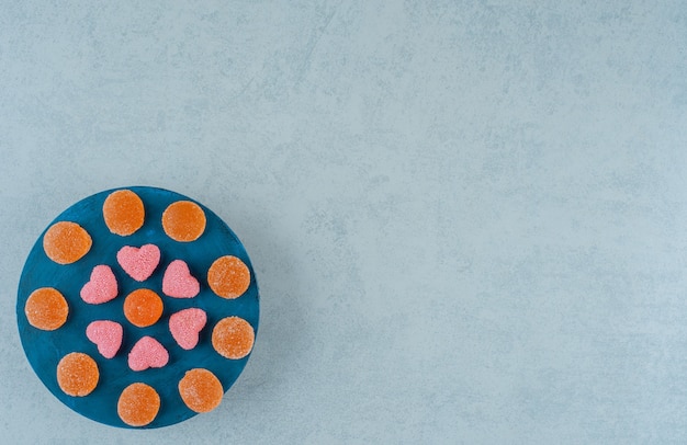 Une planche de bois bleue pleine de bonbons à la gelée sucrée orange avec des bonbons à la gelée en forme de coeur