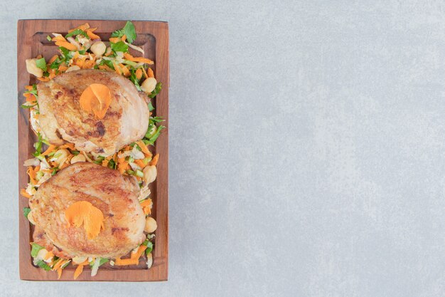 Une planche en bois avec des cuisses de poulet frites et une salade de légumes.