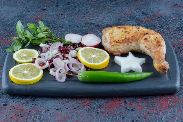 Une Planche En Bois Foncé De Légumes Et De Viande De Cuisse De Poulet