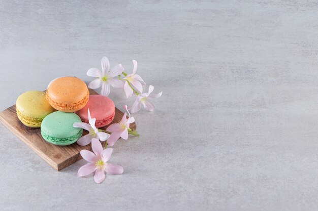 Planche de bois de macarons sucrés colorés avec des fleurs sur la surface de la pierre