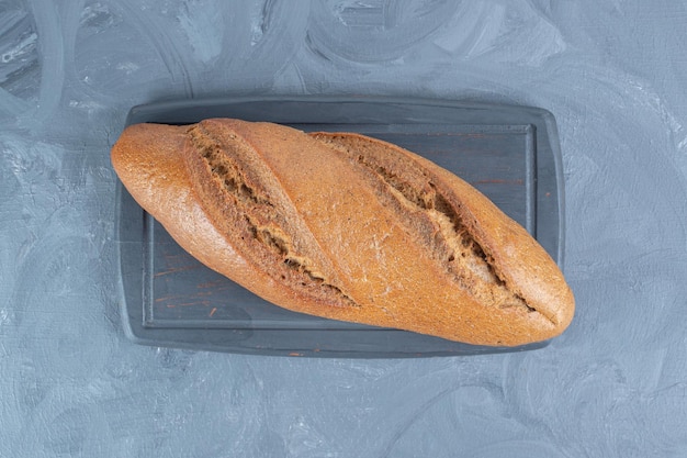 Planche de bois marine sous une seule miche de pain sur table en marbre.