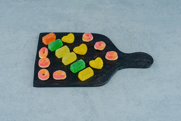 Une planche en bois noire pleine de bonbons à la gelée de fruits colorés sur une surface blanche