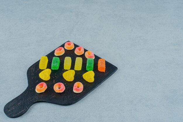 Une planche en bois noire pleine de bonbons à la gelée de fruits colorés sur une surface blanche