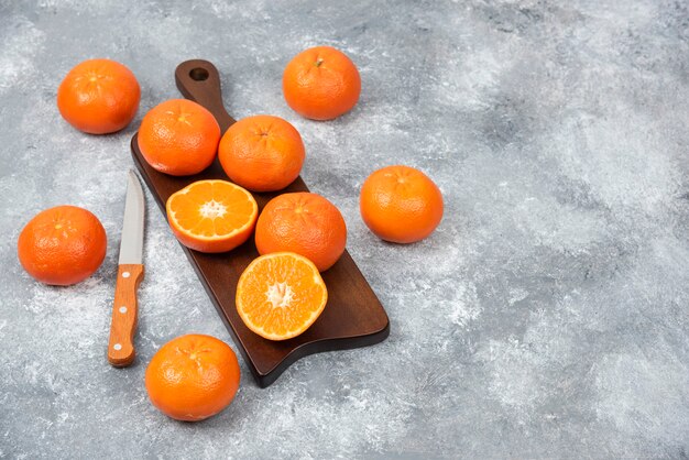 Une planche en bois pleine de fruits orange juteux avec des tranches et un couteau sur une table en pierre.