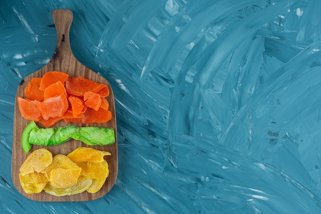 Planche de bois pleine de fruits secs sur fond bleu.