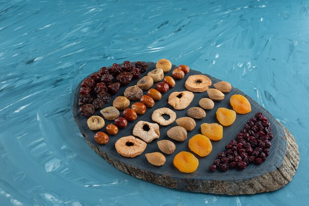 Planche de bois pleine de savoureux fruits secs sur une surface bleue.