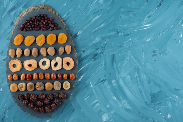 Planche De Bois Pleine De Savoureux Fruits Secs Sur Une Surface Bleue.