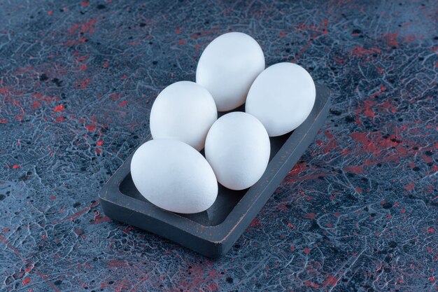 Une planche en bois sombre avec des œufs de poule blancs crus.