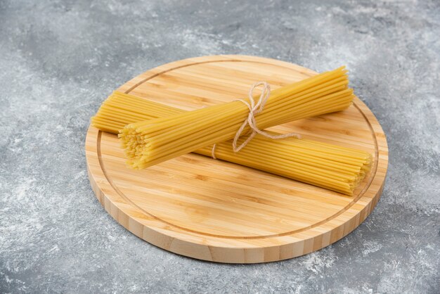 Planche de bois de spaghettis secs crus placés sur une surface en marbre.