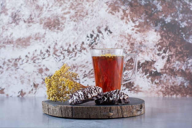 Une planche en bois d'une tasse en verre de thé chaud avec des biscuits et une fleur de mimosa