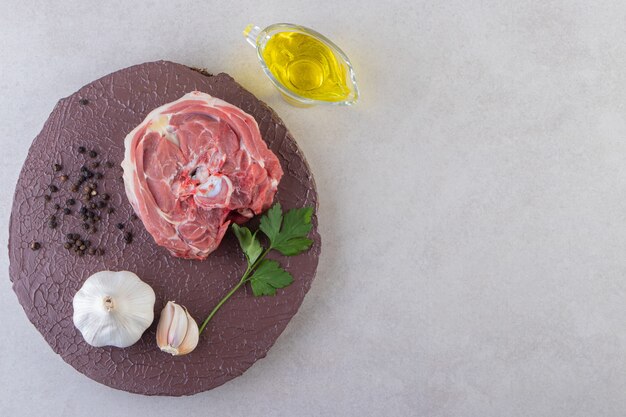 Planche de bois de viande crue avec de l'ail et de l'huile sur table.