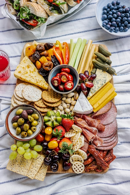 Planche de charcuterie avec de la charcuterie, des fruits frais et du fromage sur une nappe de pique-nique
