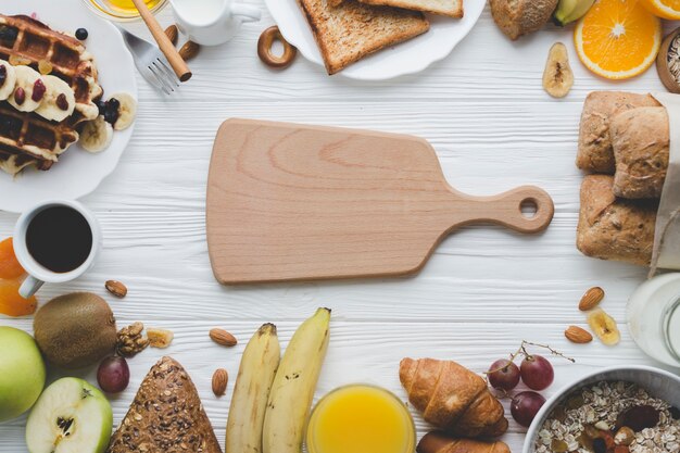 Planche à découper au milieu des fruits et de la pâtisserie