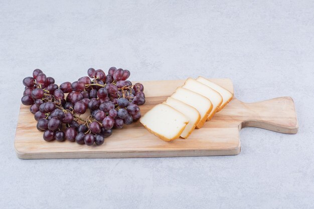 Une planche à découper en bois avec du pain tranché et des raisins. photo de haute qualité