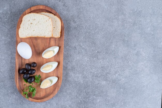 Une planche à découper en bois avec un œuf à la coque et des tranches de pain