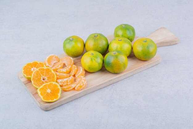 Planche à découper en bois pleine de mandarines aigres sur blanc
