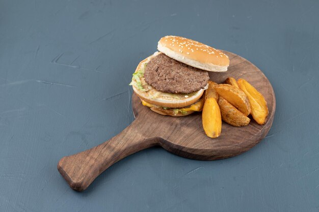 Une planche à découper en bois pleine de pommes de terre frites et de hamburger.