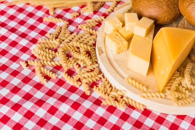 Planche à découper avec du fromage frais près du pain et des pâtes dispersées