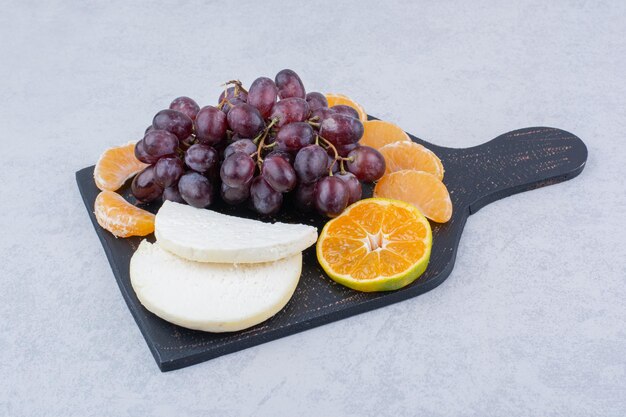 Une planche à découper sombre avec du fromage en tranches et des fruits. photo de haute qualité