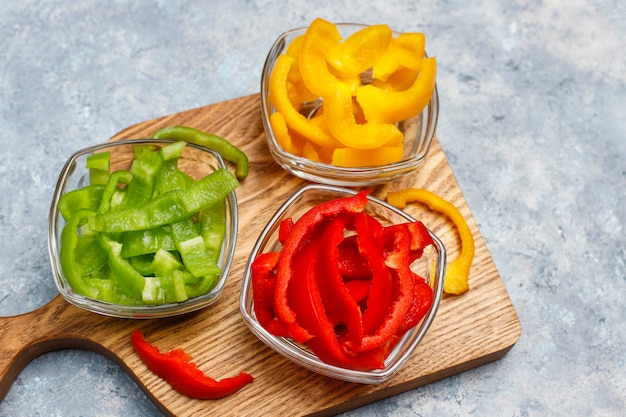 Planche à découper avec des tranches de poivrons colorés sur une surface claire. Poivrons en tranches de différentes couleurs, ingrédient de salade de légumes, cuisson des aliments sains, vue de dessus