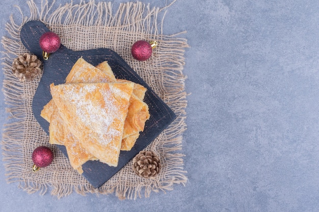 Une planche noire pleine de délicieuse tarte avec du sucre en poudre sur un sac
